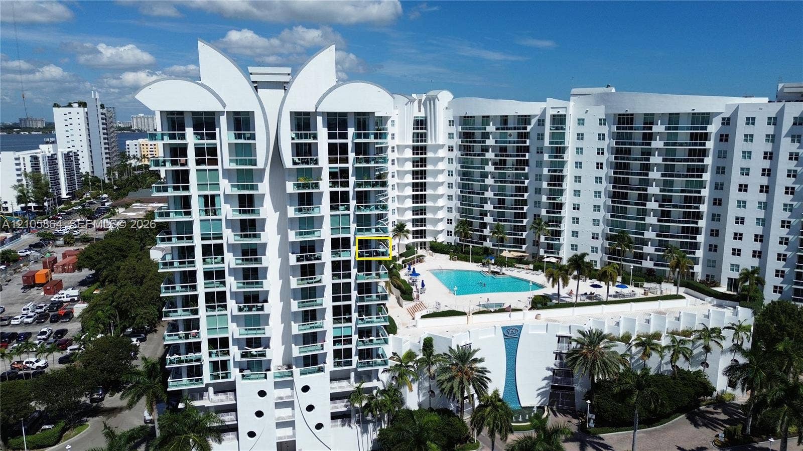 High-rise condominium building featuring tiered architectural design, private balconies, expansive ground-level swimming pool, and manicured landscaping with palm trees