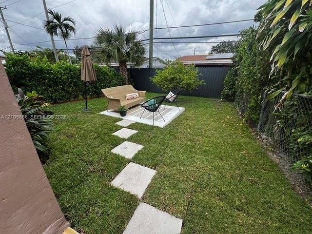 11241 SW 7th Terrace, Sweetwater, FL 33174 Private backyard featuring a manicured lawn, concrete paver pathway, elevated concrete patio, mature palms, and opaque perimeter fencing