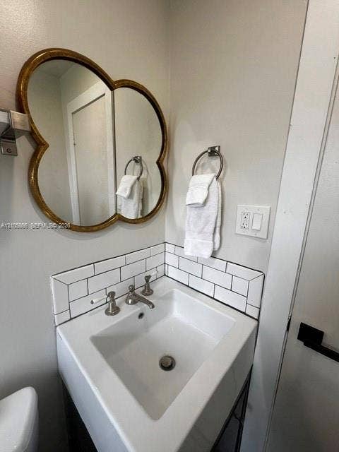 11241 SW 7th Terrace, Sweetwater, FL 33174 1/1 Private bathroom featuring a white ceramic corner sink with polished chrome faucet and fixtures, subway tile backsplash, decorative wood-framed mirror with arched detailing, and chrome towel bars