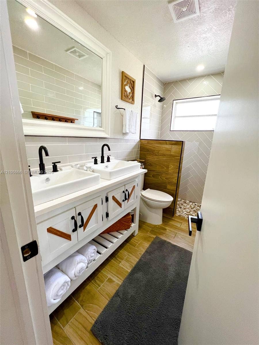 11241 SW 7th Terrace, Sweetwater, FL 33174 Main House Double vanity featuring vessel sinks, matte black hardware, wood-finish flooring, herringbone-patterned wall tile, and a walk-in shower