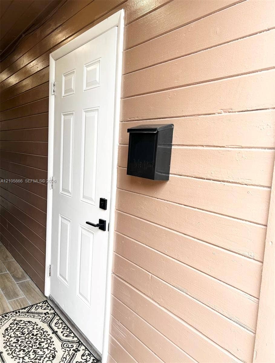 11241 SW 7th Terrace, Sweetwater, FL 33174 1/1 entry door Six-panel white entry door with matte black lever handle and electronic keypad deadbolt, complemented by horizontal lap siding and a wall-mounted metal mailbox