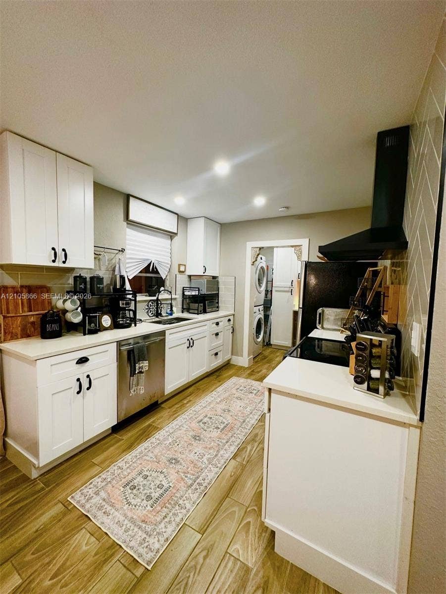 11241 SW 7th Terrace, Sweetwater, FL 33174 Main House Kitchen featuring white cabinetry, wood-finish flooring, a herringbone-patterned tile backsplash, a black range hood, and stainless steel appliances