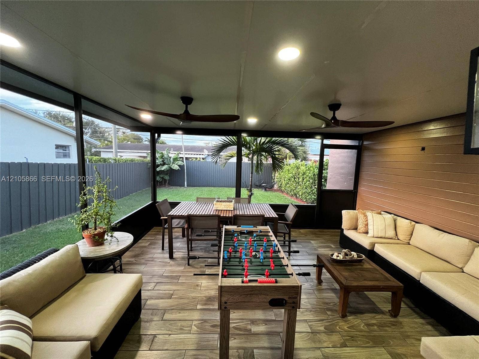 11241 SW 7th Terrace, Sweetwater, FL 33174 Main house patio and view of yard - Screened patio featuring wood-finish tile flooring, horizontal slat wall paneling, dual ceiling fans, and integrated recessed lighting