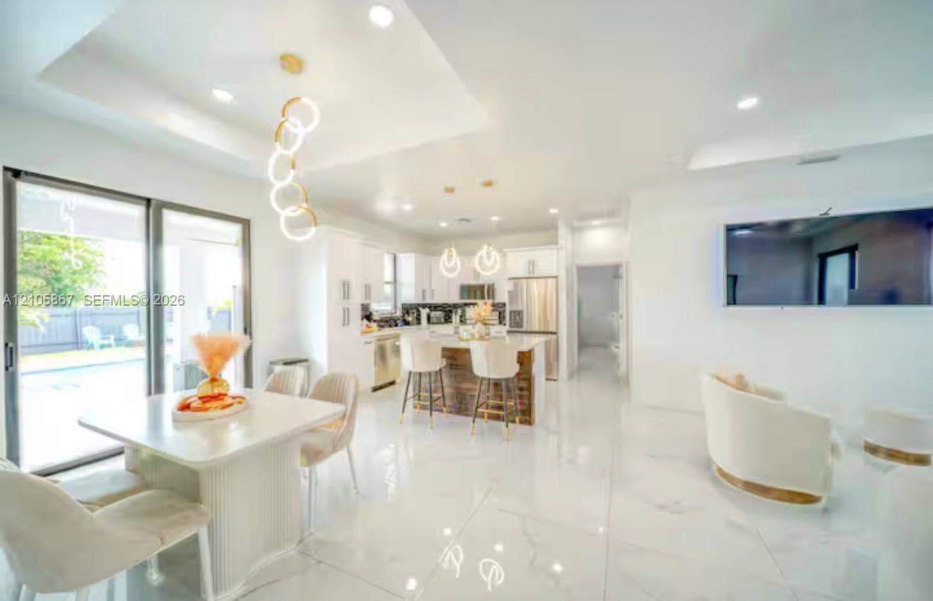 Open-concept space featuring polished stone-finish flooring, tray ceilings with recessed lighting, a modern center island with stone countertop, stainless steel appliances, and large sliding glass doors
