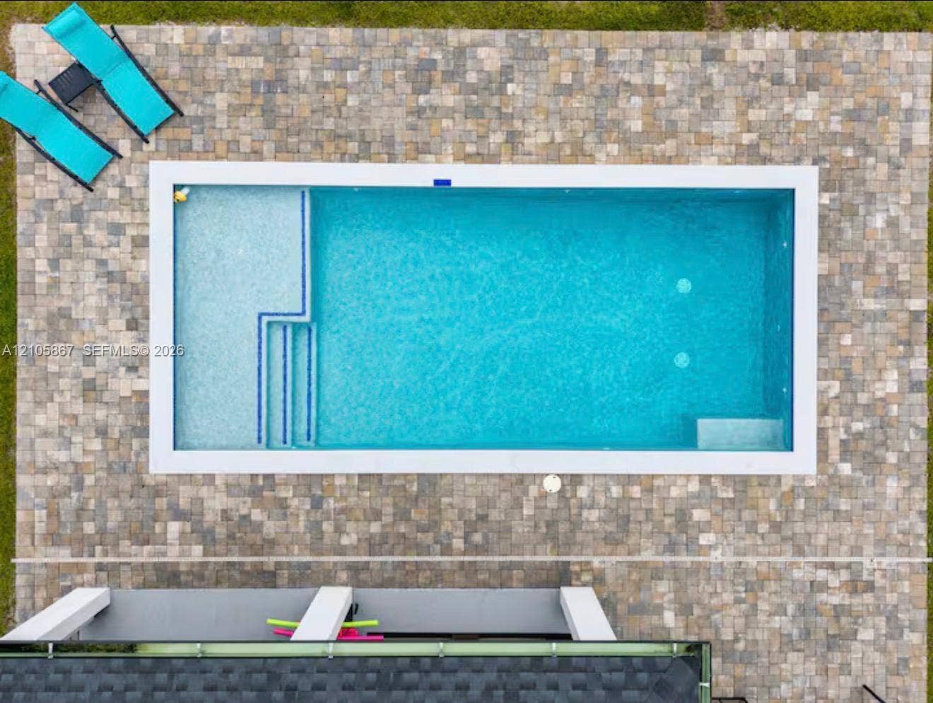 Rectangular swimming pool featuring a tiled interior, integrated entry steps, a built-in sun shelf, and a perimeter stone paver patio