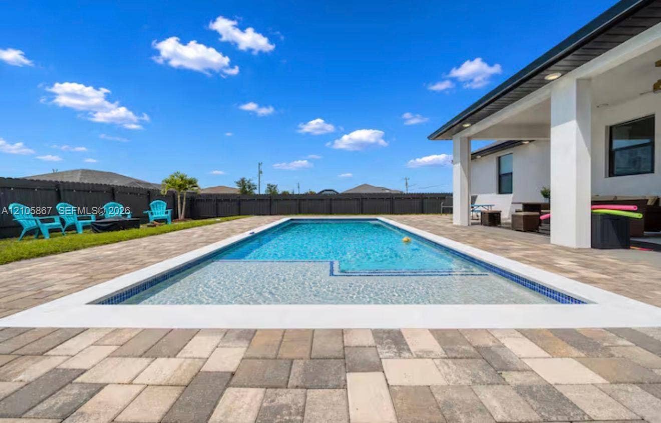 Rectangular in-ground pool featuring a shallow tanning ledge, surrounding paver patio, covered porch, and dark wood-tone privacy fencing