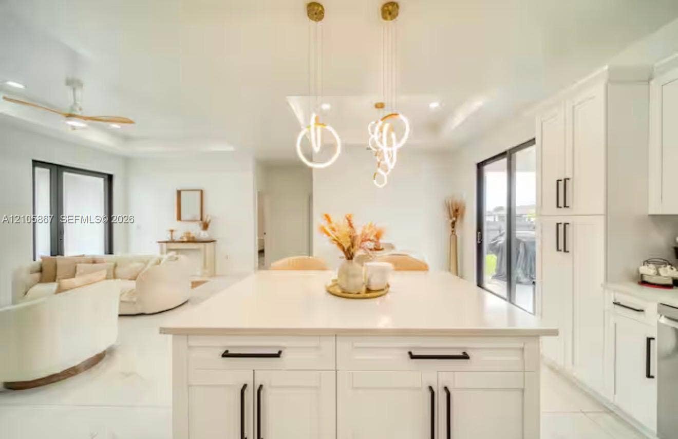 Kitchen featuring an expansive center island with solid-surface countertop, white Shaker-style cabinetry, matte black hardware, and contemporary ring pendant lighting