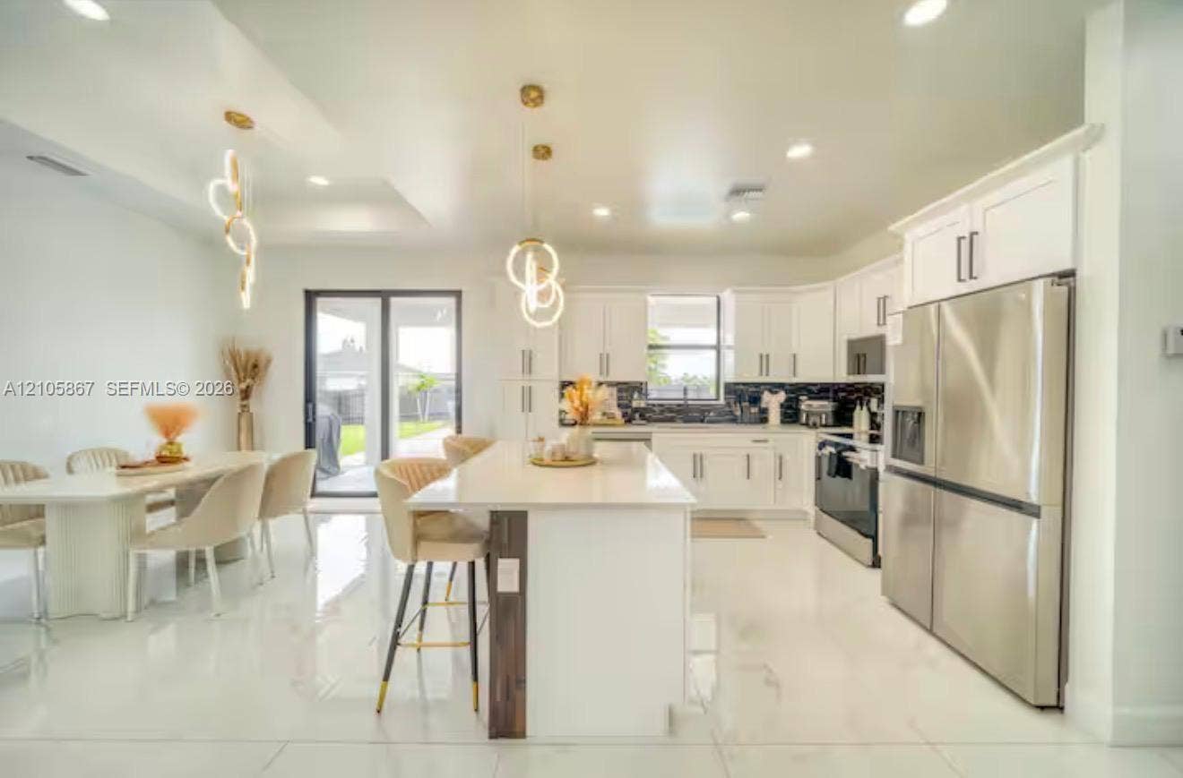 Kitchen featuring white shaker-style cabinetry, quartz countertops, central island, stainless steel appliances, and large-format tile flooring
