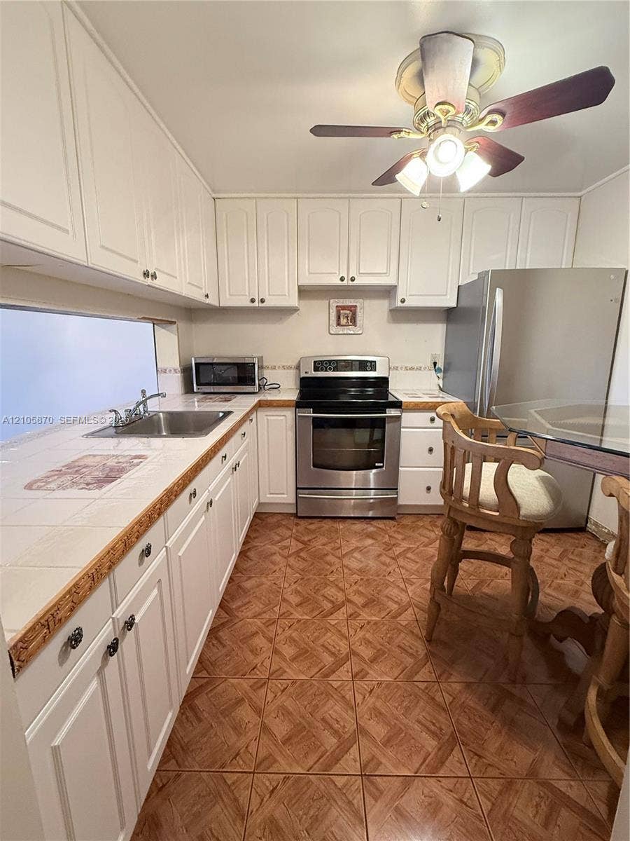 7173 Orange Drive, #204B, Davie, FL 33314 Kitchen featuring white cabinetry, tile countertops, stainless steel appliances, a stainless steel sink with a dual-handle faucet, and tile flooring