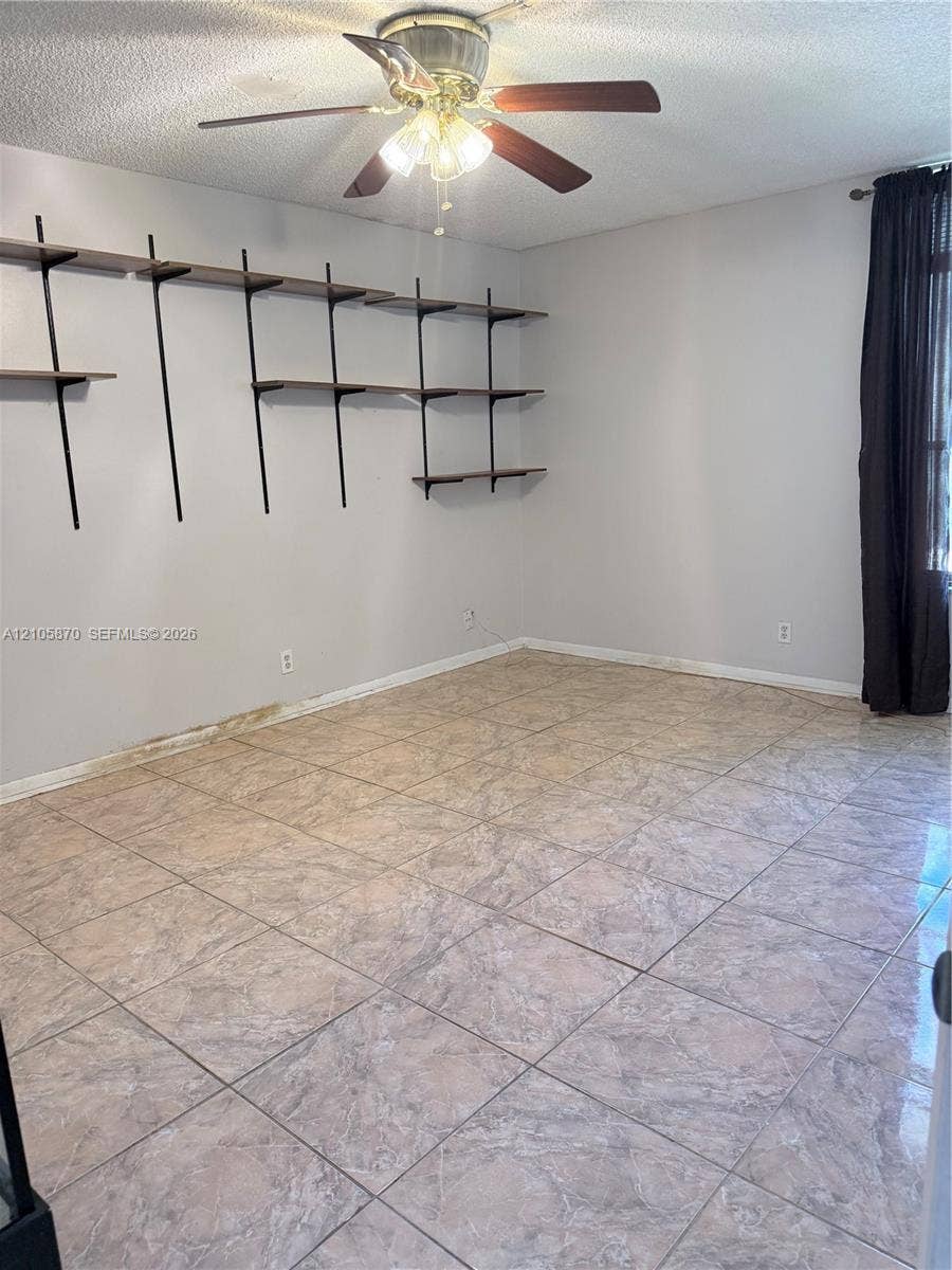 7173 Orange Drive, #204B, Davie, FL 33314 Room featuring large-format ceramic tile flooring, wall-mounted tiered shelving, and a ceiling fan with integrated lighting