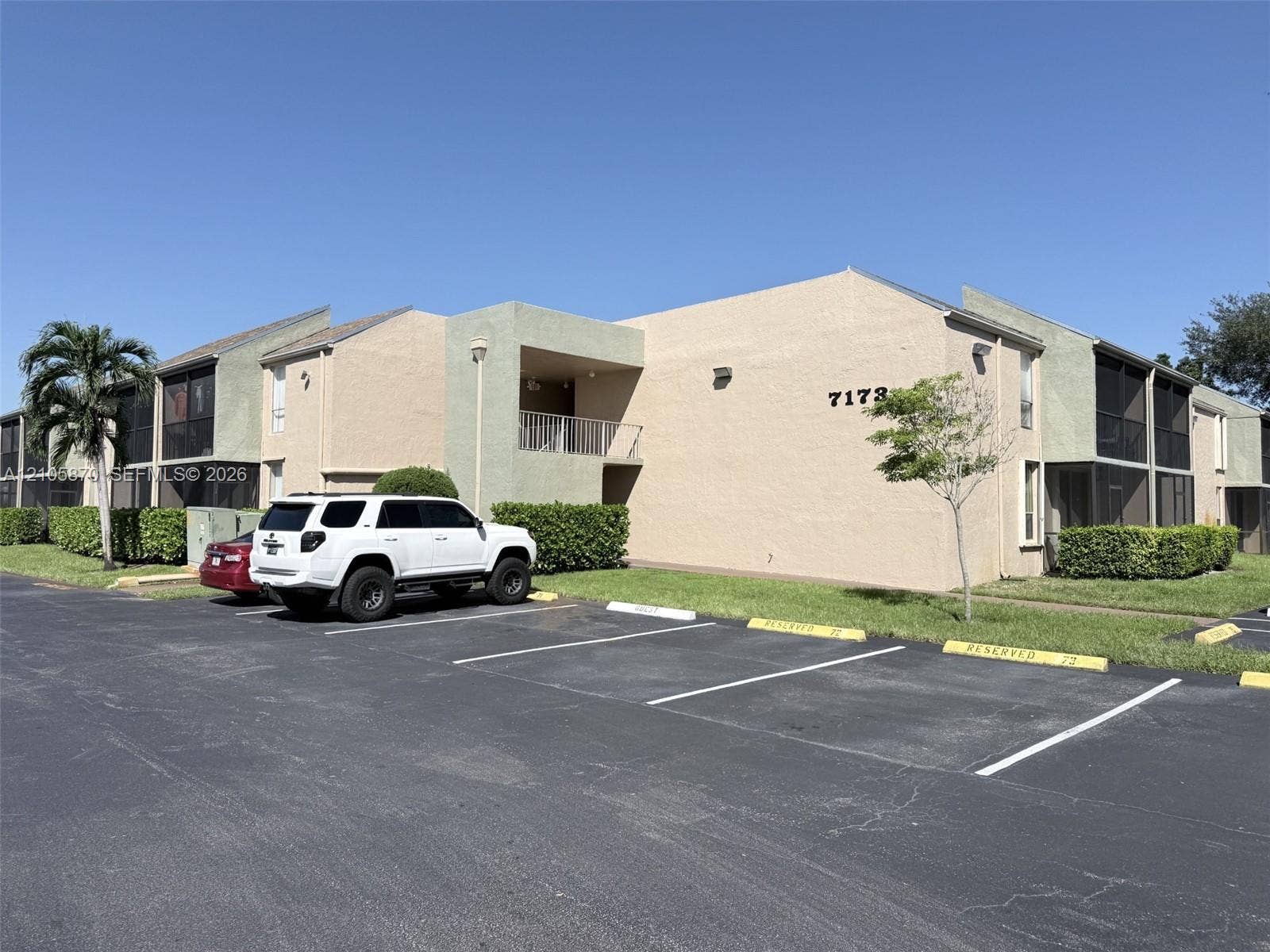 7173 Orange Drive, #204B, Davie, FL 33314 Multi-level exterior featuring a stucco facade, covered balconies, screened enclosures, and asphalt parking area
