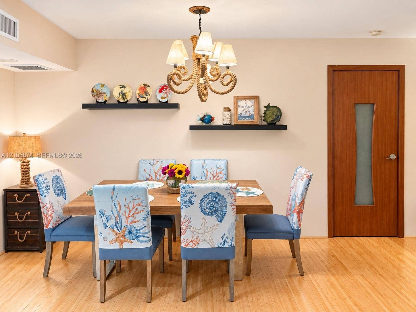 Dining area featuring hardwood flooring, rope-wrapped chandelier, dual floating wall shelves, and a wooden door with a frosted glass panel insert