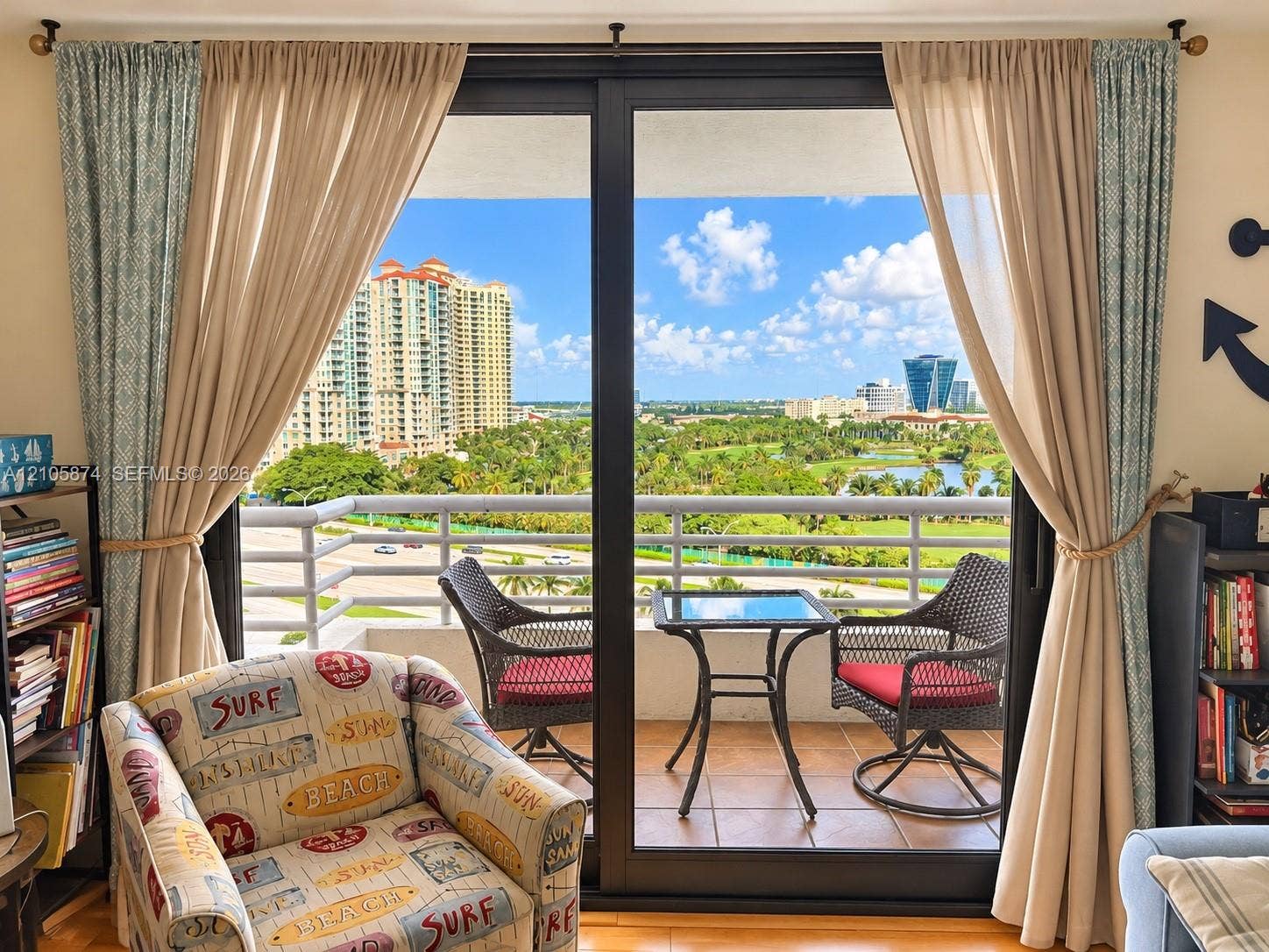 Large black-framed sliding glass doors opening to a balcony with metal railings and tile flooring, featuring an expansive skyline and landscape backdrop