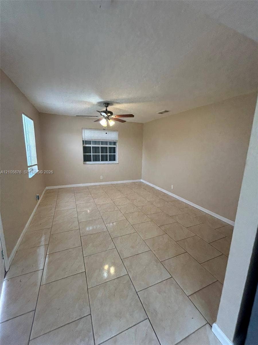 Riviera Beach, Riviera Beach, FL 33404 Neutral-toned room featuring large-format ceramic tile flooring, multi-pane windows, and a central ceiling fan with integrated lighting