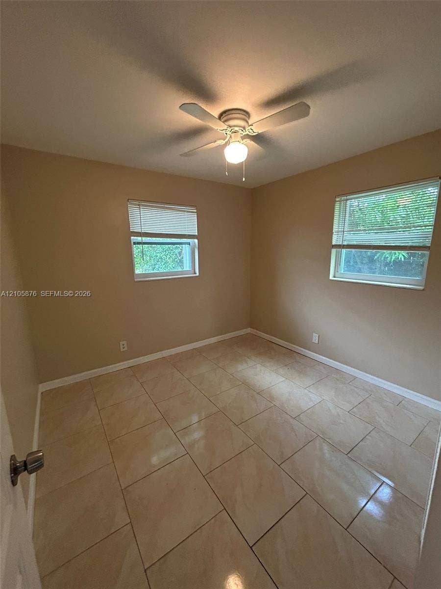 Riviera Beach, Riviera Beach, FL 33404 Neutral-toned interior featuring large-format tile flooring, dual windows with blinds, and a central ceiling fan with integrated lighting