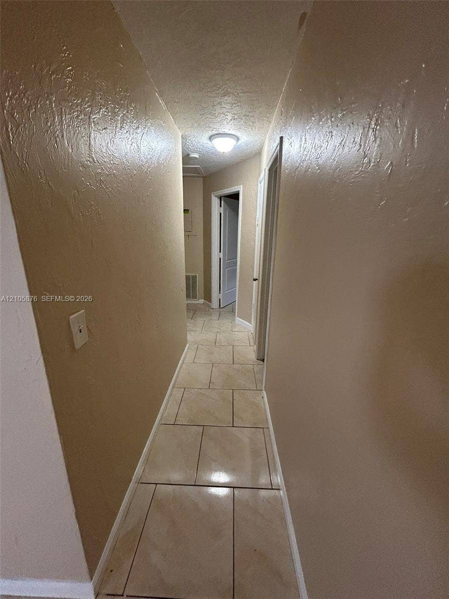 Riviera Beach, Riviera Beach, FL 33404 Hallway featuring neutral-toned textured wall finishes and large-format ceramic tile flooring with an integrated flush-mount ceiling light fixture