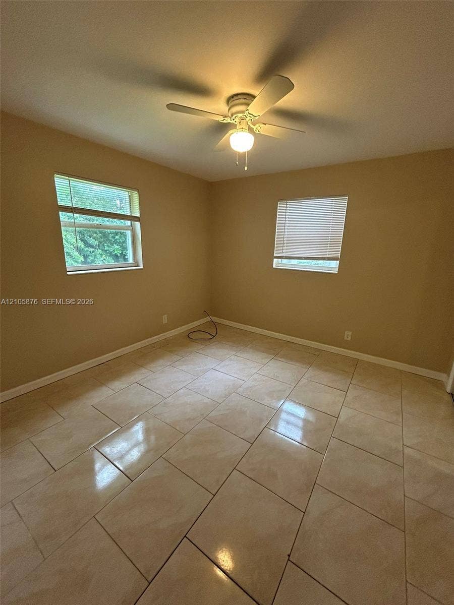 Riviera Beach, Riviera Beach, FL 33404 Room featuring large-format neutral tile flooring, two windows with blinds, and a central ceiling fan with an integrated light fixture