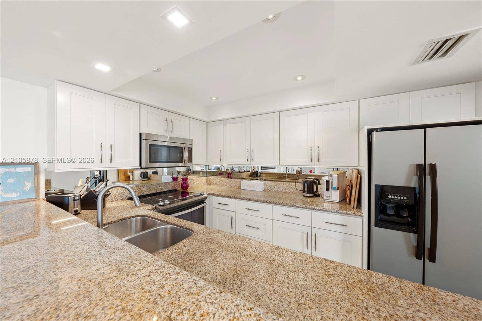 650 West Avenue, #1807, Miami Beach, FL 33139 Kitchen featuring white shaker-style cabinetry, expansive stone countertops, stainless steel appliances, a double-basin undermount sink, and mirrored backsplash