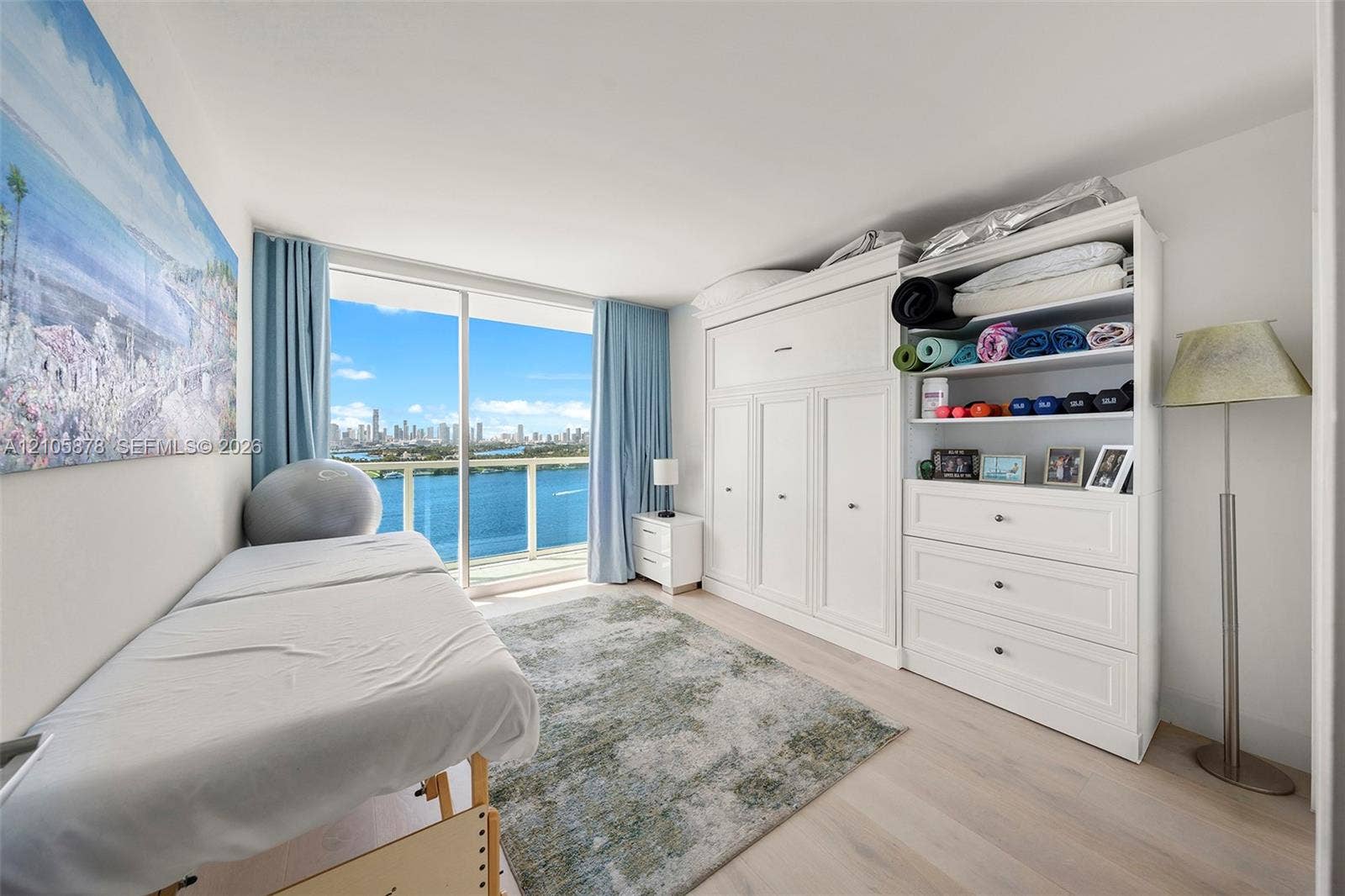 650 West Avenue, #1807, Miami Beach, FL 33139 Floor-to-ceiling sliding glass door, custom built-in white cabinetry with integrated shelving and drawers, wood-finish flooring, and coastal skyline horizon