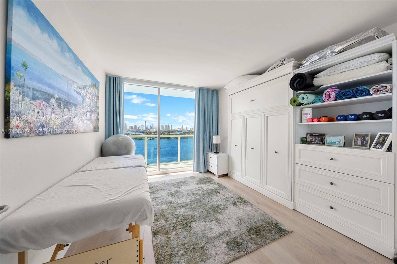 650 West Avenue, #1807, Miami Beach, FL 33139 Floor-to-ceiling sliding glass door, custom built-in white cabinetry, wood-finish flooring, and expansive water and skyline backdrop
