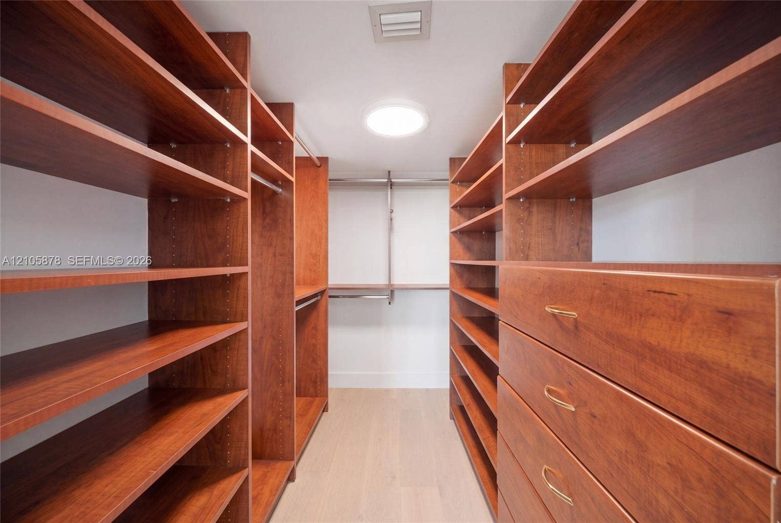 650 West Avenue, #1807, Miami Beach, FL 33139 Walk-in storage space featuring extensive custom wood-finish shelving, integrated clothing rods, built-in dresser drawers with metallic pulls, and light-toned flooring