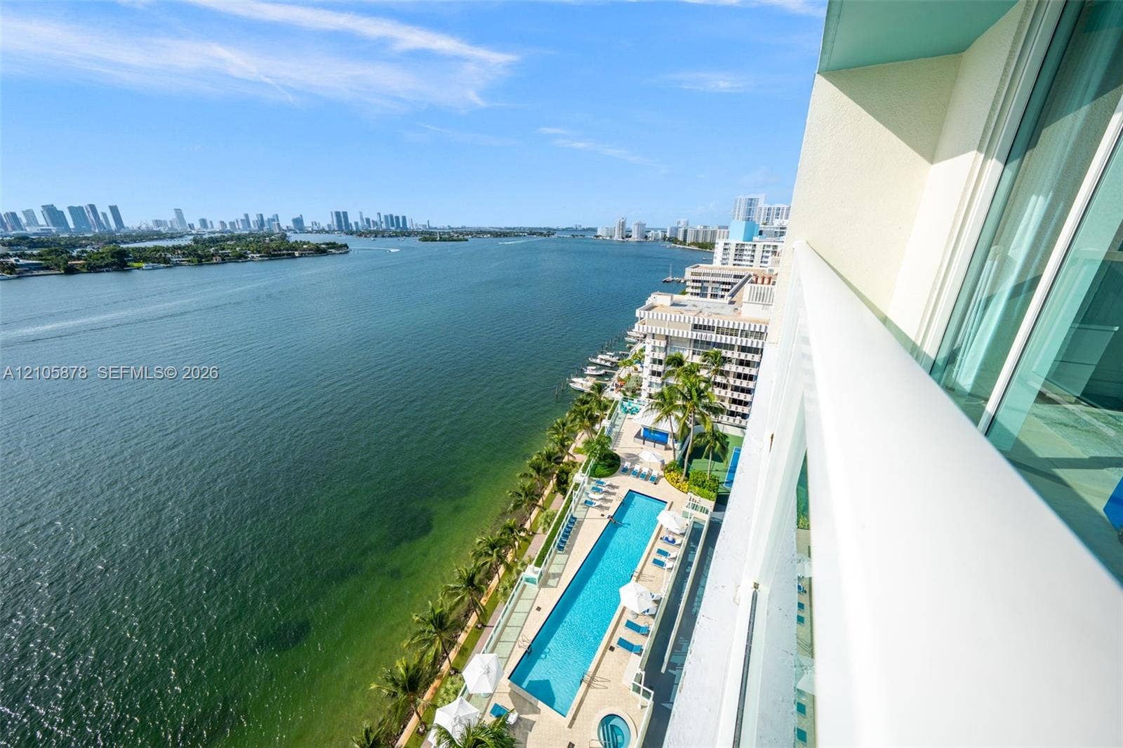 650 West Avenue, #1807, Miami Beach, FL 33139 Private balcony with glass railing, overlooking an outdoor swimming pool, hot tub, manicured palm landscaping, and expansive waterfront