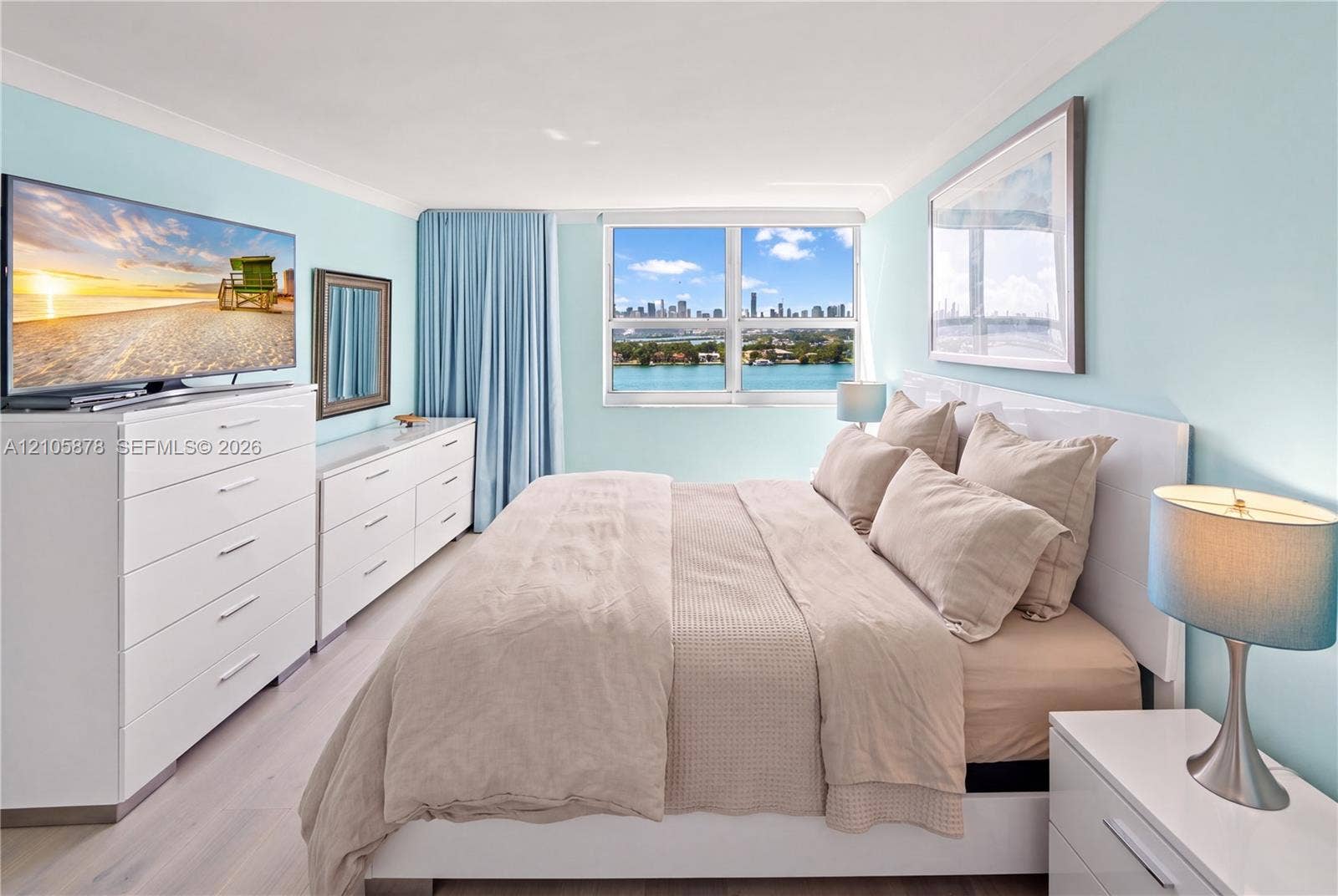 650 West Avenue, #1807, Miami Beach, FL 33139 Bedroom featuring light-toned wood-finish flooring, a large window with cityscape and water scenery, and a bright, neutral color palette