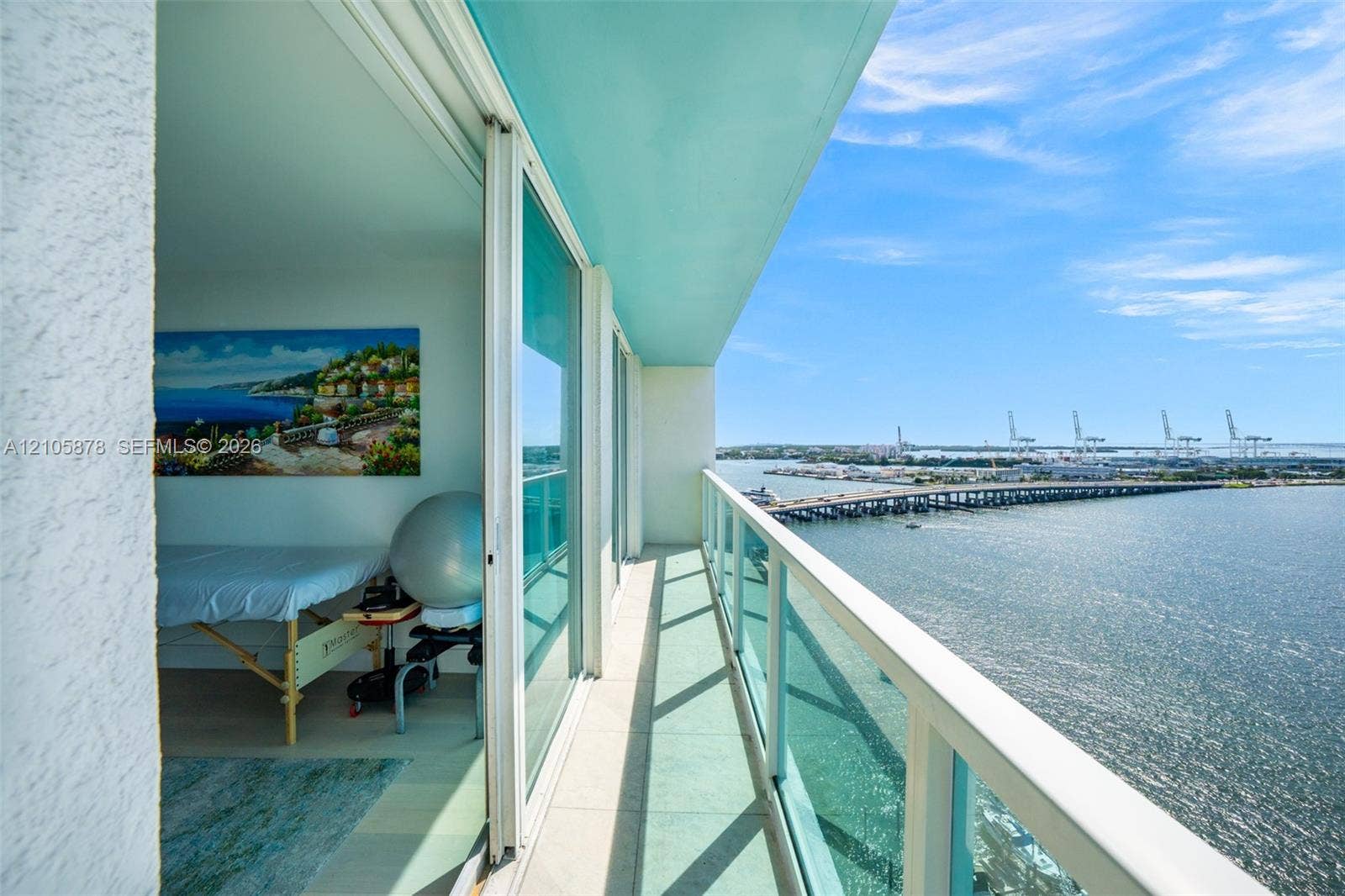 650 West Avenue, #1807, Miami Beach, FL 33139 Covered balcony with a glass panel railing, featuring large sliding glass doors and neutral tile flooring