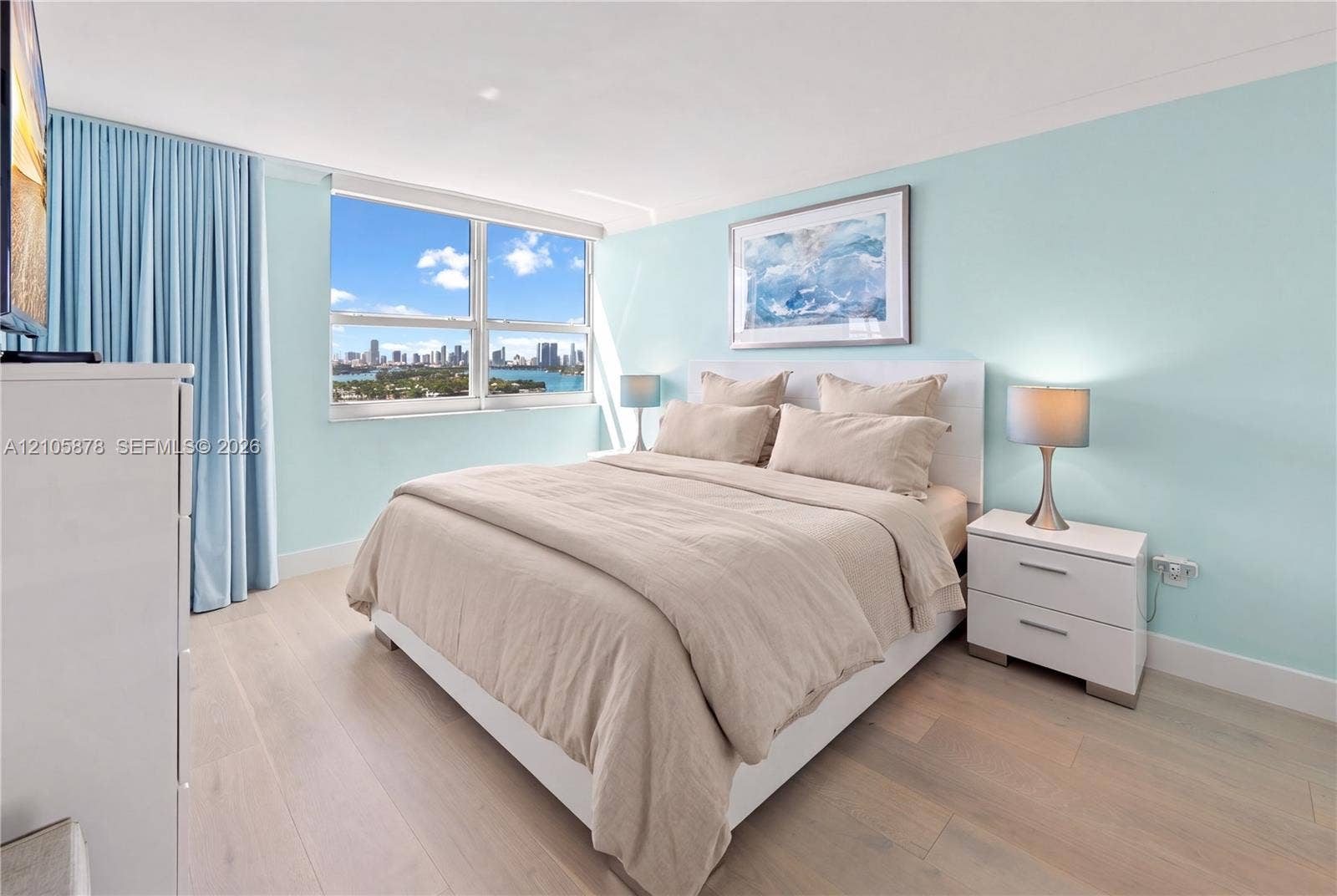 650 West Avenue, #1807, Miami Beach, FL 33139 Room featuring light-toned wood-finish flooring, floor-to-ceiling drapery, and a large window showcasing a city skyline and water