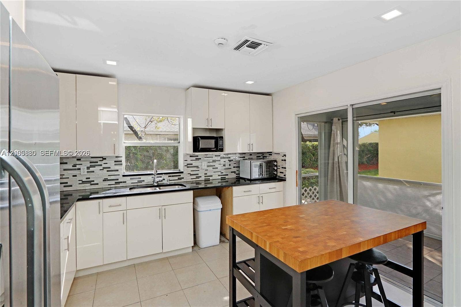 527 SE 21st Drive, Homestead, FL 33033 Kitchen featuring high-gloss cabinetry, stone-finish countertops, geometric tile backsplash, tile flooring, and a butcher-block topped center island