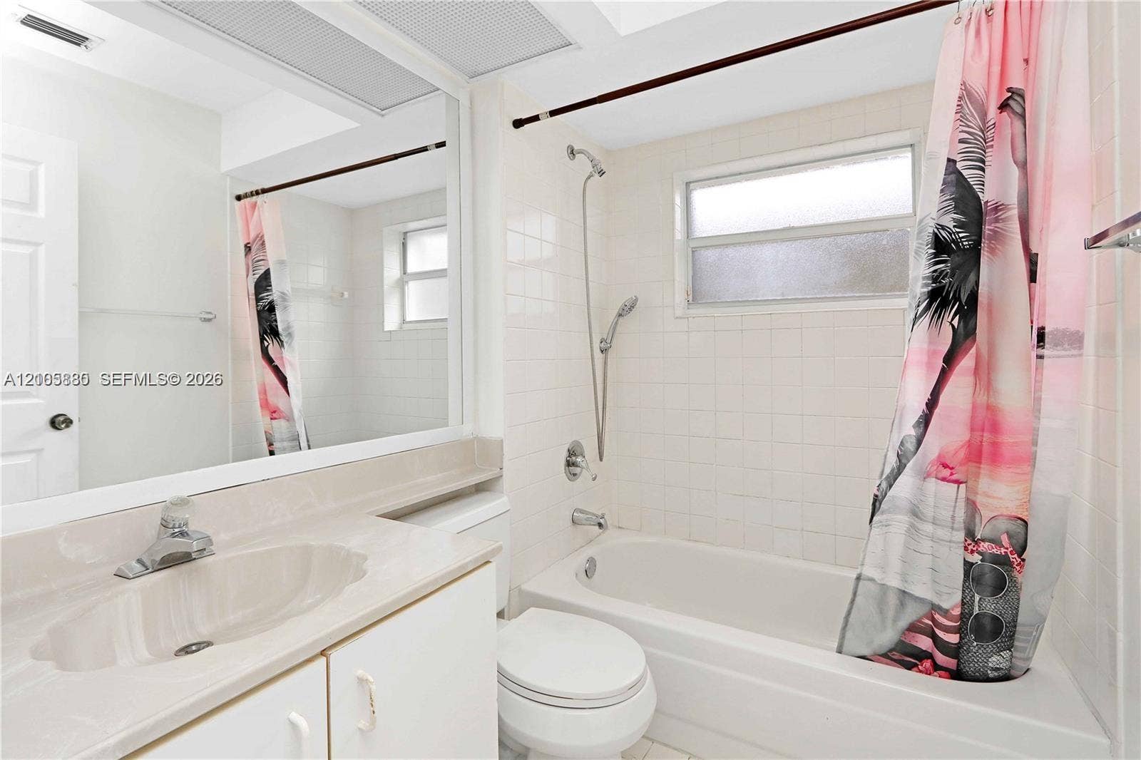527 SE 21st Drive, Homestead, FL 33033 Full-width vanity with an integrated sink, expansive wall-mounted mirror, white ceramic tile shower surround, and a handheld shower fixture