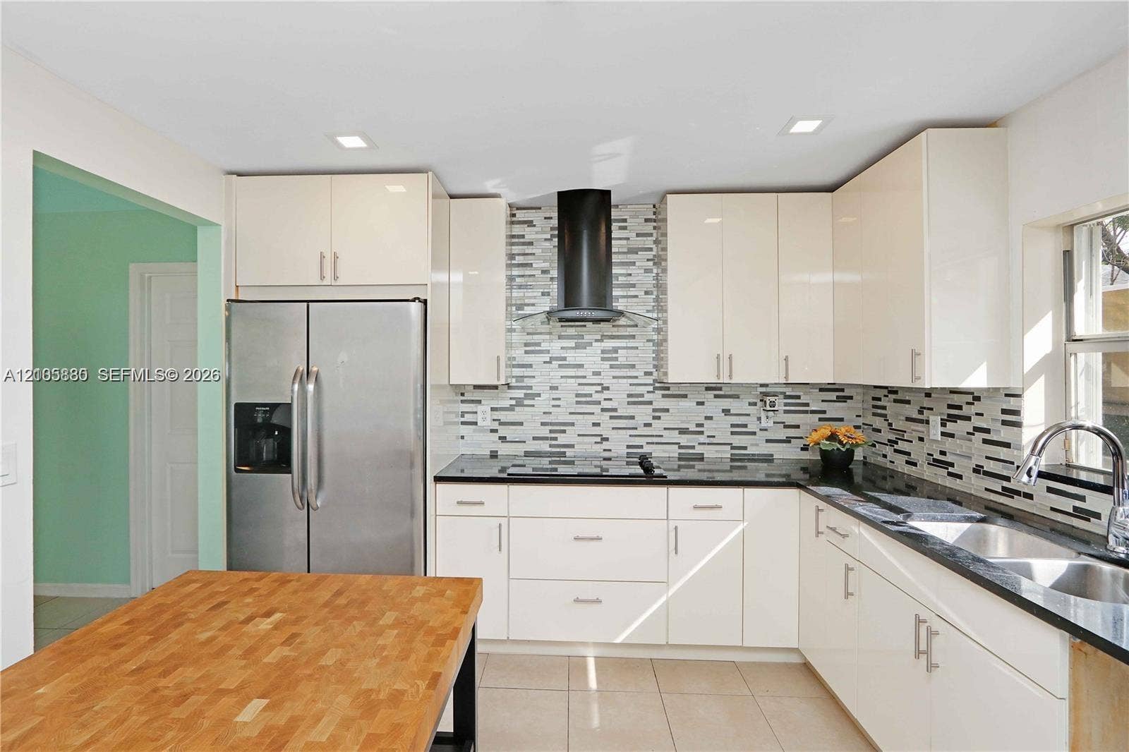 527 SE 21st Drive, Homestead, FL 33033 Kitchen featuring high-gloss cabinetry, stone countertops, a multi-tonal mosaic tile backsplash, stainless steel appliances, and a black range hood