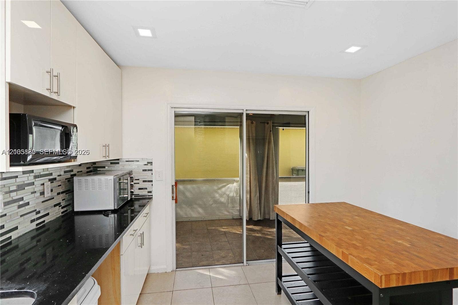 527 SE 21st Drive, Homestead, FL 33033 Kitchen featuring flat-panel cabinetry, black countertops, multi-toned mosaic tile backsplash, recessed lighting, and sliding glass doors