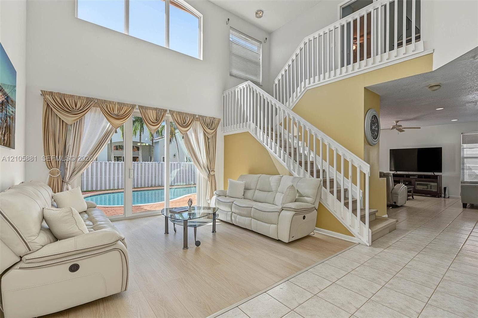 1588 SW 191st Avenue, Pembroke Pines, FL 33029 Double-height living area featuring floor-to-ceiling windows, wood-finish flooring, sliding glass doors, and a white wood-railing staircase