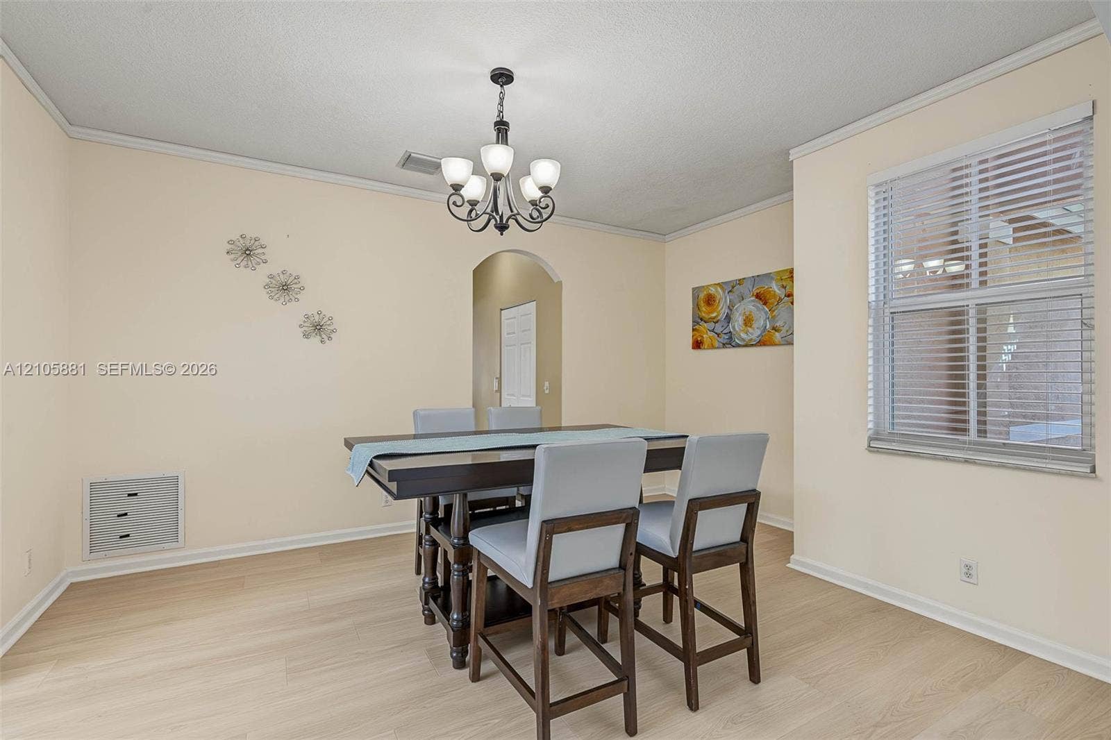 1588 SW 191st Avenue, Pembroke Pines, FL 33029 Dining area featuring light-toned wood-finish flooring, a wrought iron chandelier with frosted glass shades, crown molding, and an arched entryway