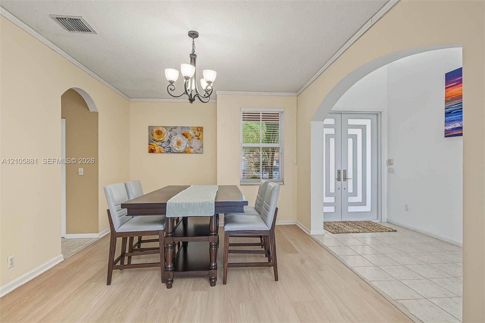 1588 SW 191st Avenue, Pembroke Pines, FL 33029 Dining area featuring wood-finish flooring, a decorative chandelier, and crown molding, accented by a distinctive arched entryway leading to double front doors with geometric glass inlays