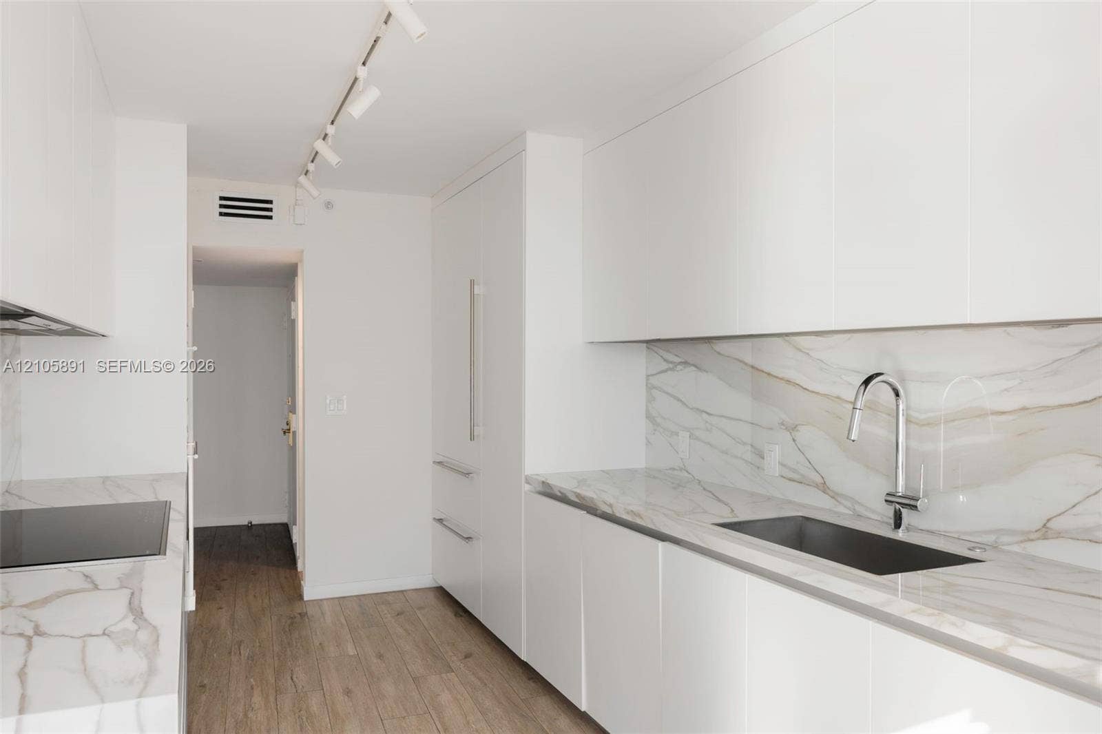 9 Island Avenue, #1215, Miami Beach, FL 33139 Modern kitchen featuring white flat-panel cabinetry, stone-finish countertops and backsplash, integrated refrigerator, undermount sink with high-arc faucet, and wood-finish flooring
