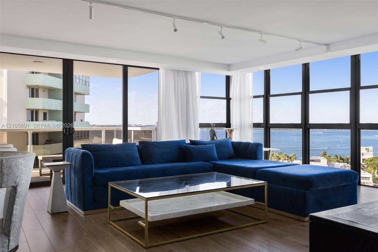 9 Island Avenue, #1215, Miami Beach, FL 33139 Floor-to-ceiling windows with black metal frames, wood-finish flooring, ceiling-mounted track lighting, and a sliding glass door opening to a private balcony