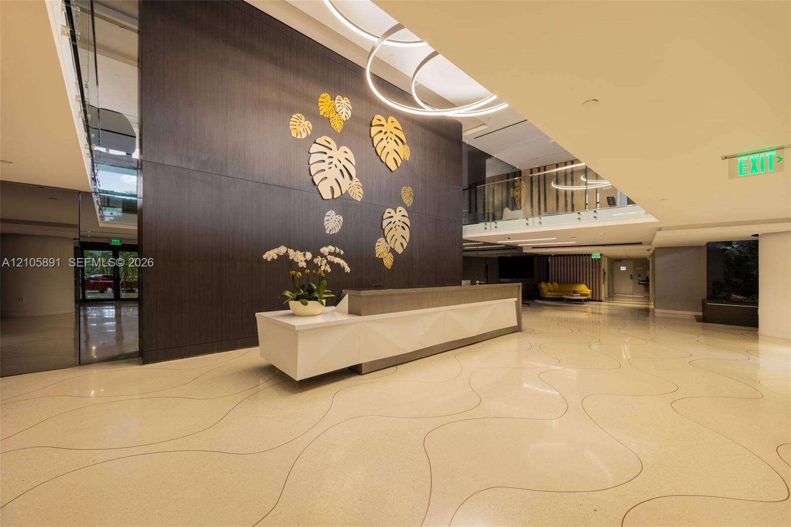 9 Island Avenue, #1215, Miami Beach, FL 33139 Lobby featuring high-gloss flooring with inlaid curvilinear detailing, a dark-finish wood-paneled accent wall with metallic leaf-shaped wall art, a structured white reception desk, and circular architectural light fixtures