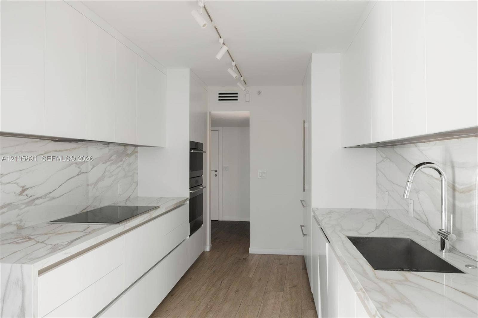 9 Island Avenue, #1215, Miami Beach, FL 33139 Galley kitchen featuring flat-panel white cabinetry, stone-surface countertops and backsplashes, built-in dual ovens, integrated cooktop, and wood-finish flooring