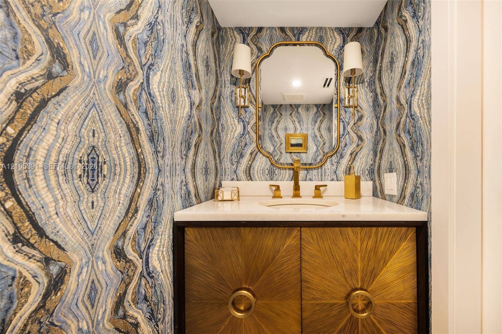 9 Island Avenue, #1215, Miami Beach, FL 33139 Custom vanity with metallic-textured cabinetry, stone countertop, integrated undermount sink, brass-finish fixtures, and designer wallpaper