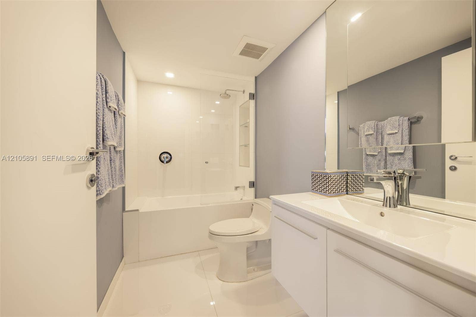9 Island Avenue, #1215, Miami Beach, FL 33139 Bathroom featuring a white vanity with an integrated sink, a large wall-mounted mirror, a tub-shower combination with a glass panel, and polished tile flooring