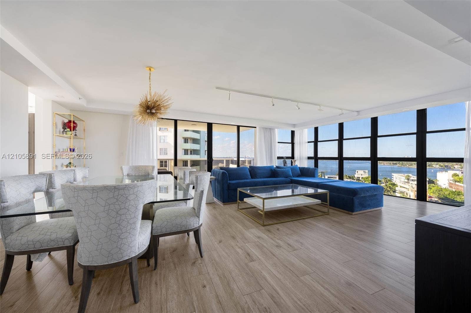 9 Island Avenue, #1215, Miami Beach, FL 33139 Open-concept living space featuring wood-finish flooring, floor-to-ceiling black-framed windows, and a decorative gold-finish pendant light
