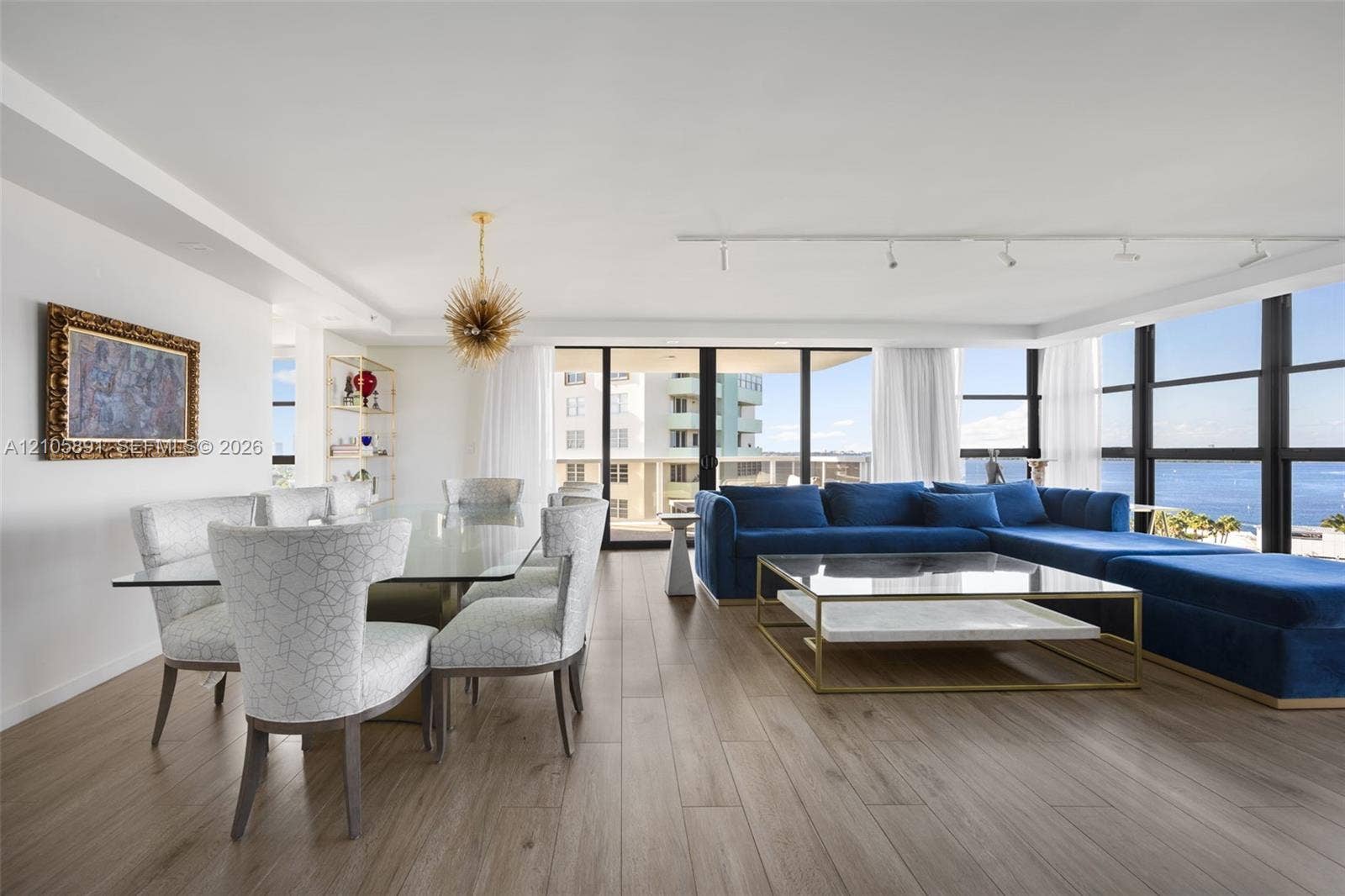 9 Island Avenue, #1215, Miami Beach, FL 33139 Open-concept interior featuring wood-finish flooring, floor-to-ceiling windows with water vistas, built-in recessed display shelving, and modern track lighting