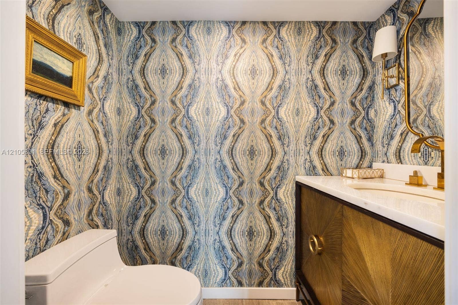 9 Island Avenue, #1215, Miami Beach, FL 33139 Powder room featuring patterned wallpaper, a wood-finish vanity with sunburst detailing, a stone-composite countertop, an integrated sink, and brass-finish fixtures