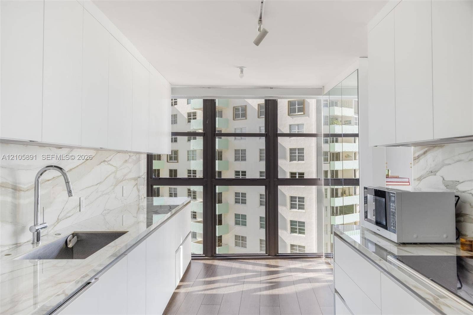 9 Island Avenue, #1215, Miami Beach, FL 33139 Kitchen featuring white flat-panel cabinetry, floor-to-ceiling windows, veined stone-finish countertops and backsplash, wood-finish flooring, and a stainless steel undermount sink with a gooseneck faucet