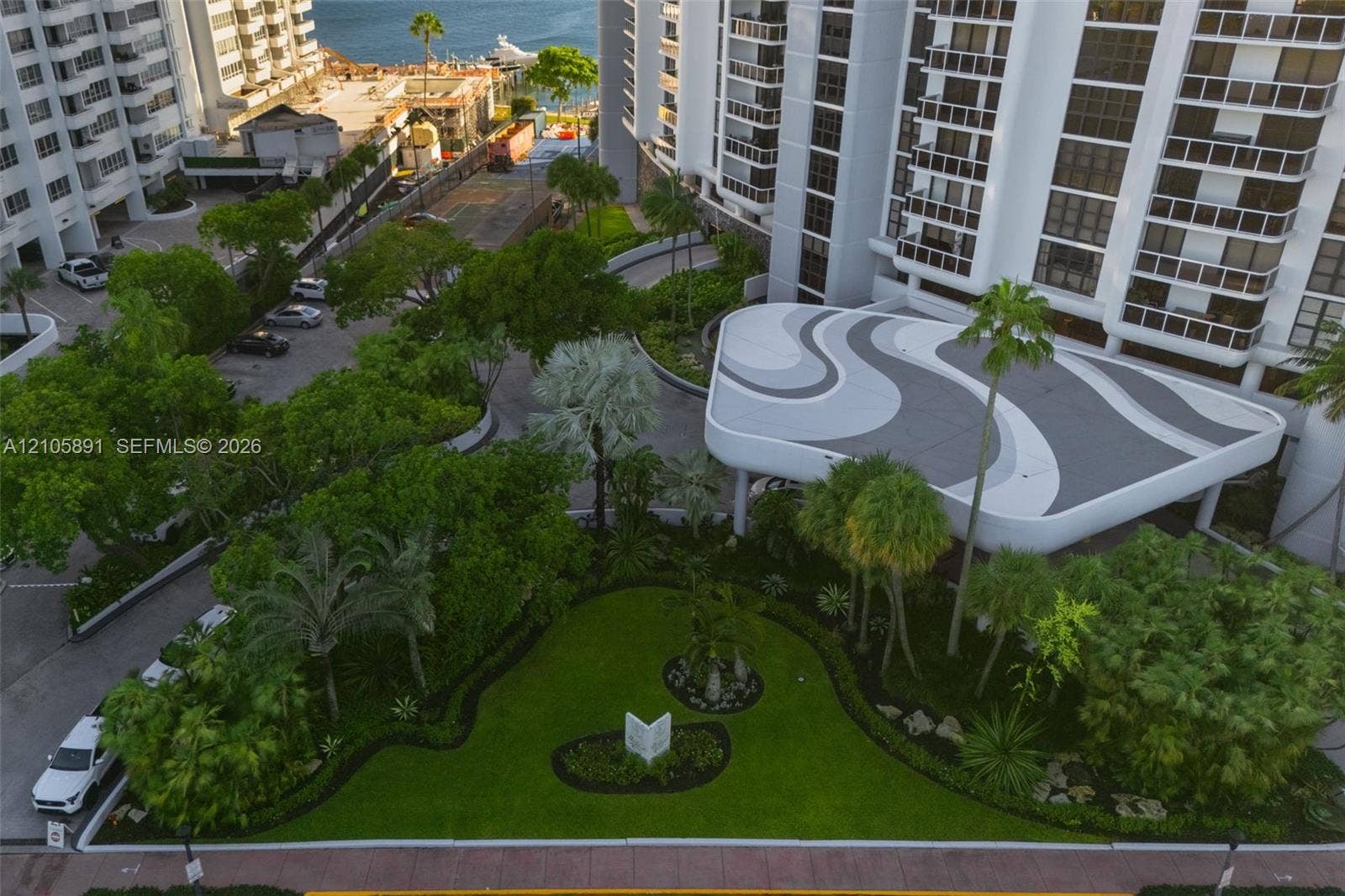 9 Island Avenue, #1215, Miami Beach, FL 33139 High-rise exterior featuring a patterned porte-cochre, manicured landscaping, mature trees, and paved motor court