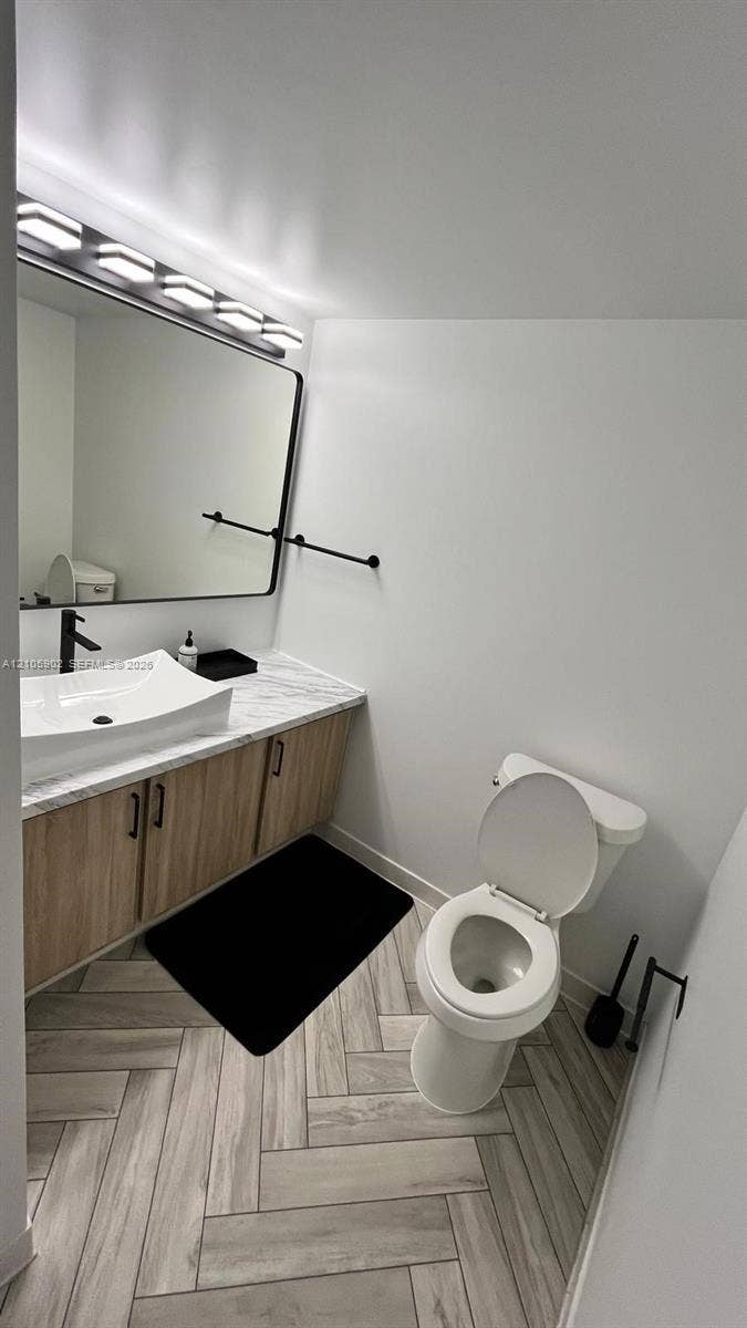 600 Three Islands Boulevard, #913, Hallandale Beach, Hallandale Beach, FL 33009 Bathroom featuring wood-finish cabinetry, stone-patterned vanity countertop with a vessel sink, matte black hardware, and herringbone-patterned flooring