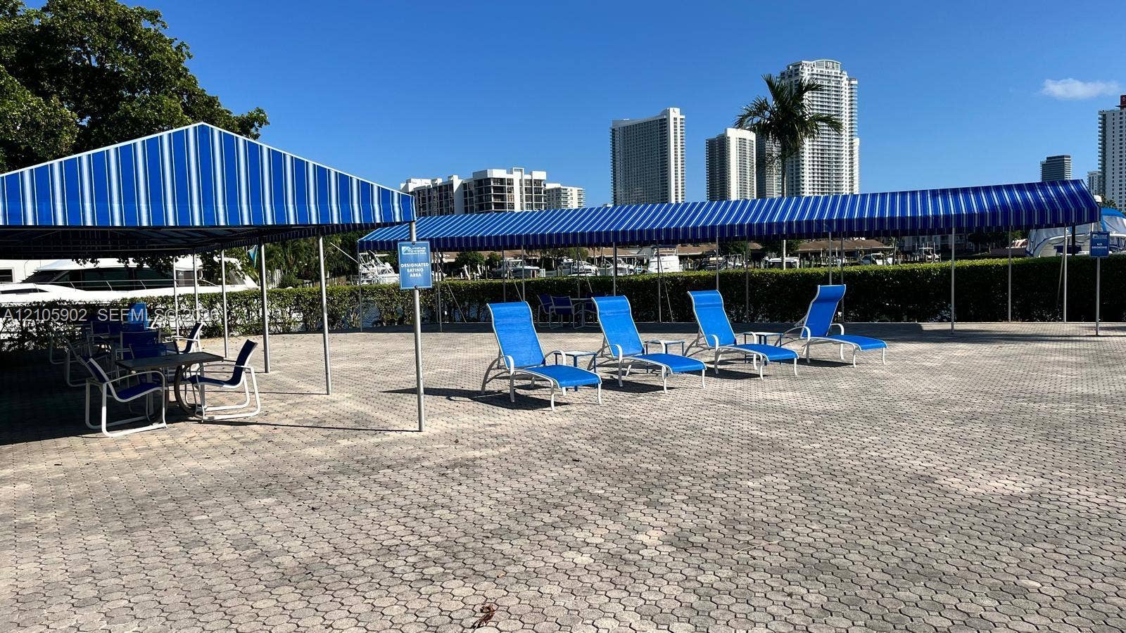 600 Three Islands Boulevard, #913, Hallandale Beach, Hallandale Beach, FL 33009 Outdoor paved patio area featuring extensive striped retractable awnings, perimeter privacy hedges, and paved stone surfacing