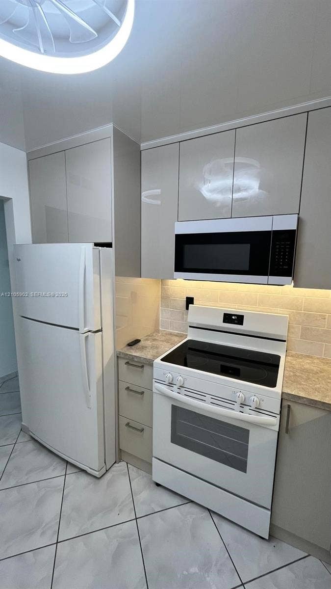 600 Three Islands Boulevard, #913, Hallandale Beach, Hallandale Beach, FL 33009 Kitchen featuring glossy, flat-panel cabinetry, stone-finish countertops, subway tile backsplash, and ceramic tile flooring